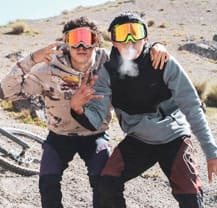 Disfrutando en un restaurante al aire libre en una tarde soleada. Persona con barba y gafas, con camiseta de Deftones, sosteniendo una carta.